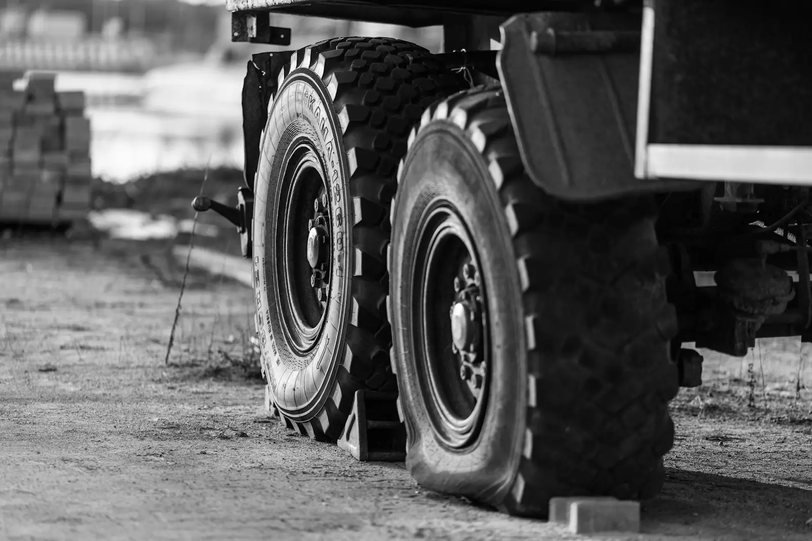 Close-up of the heavy double tires of a large dump truck on a sandy industrial road. Black-and-white study of working machinery.