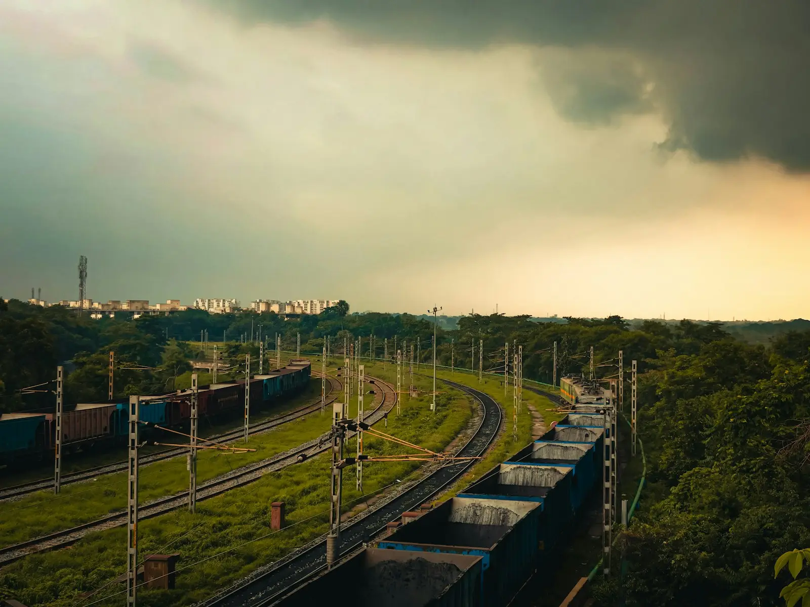 Freight trains on curved tracks through a green landscape under a stormy sky