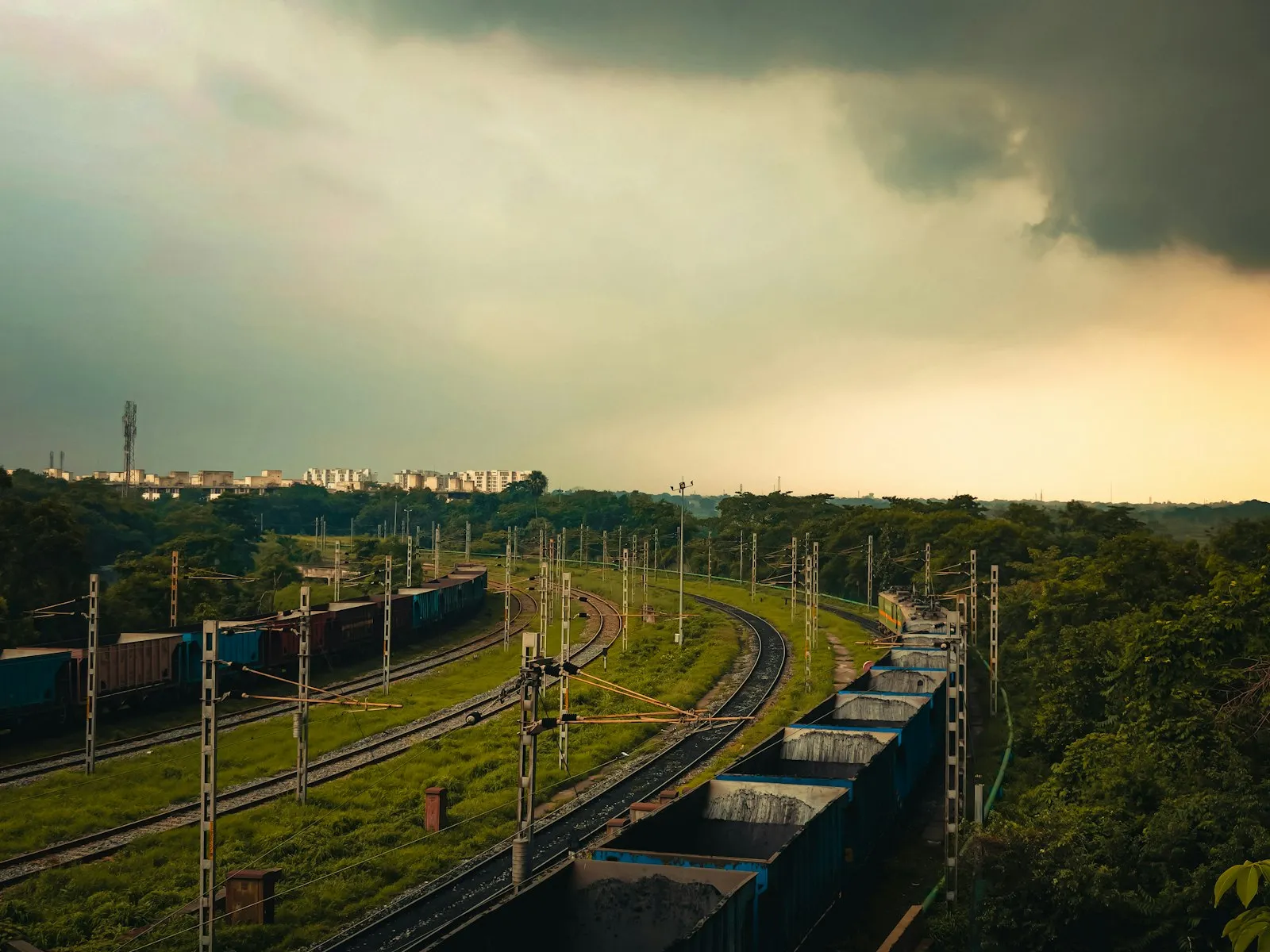 Freight trains on curved tracks through a green landscape under a stormy sky