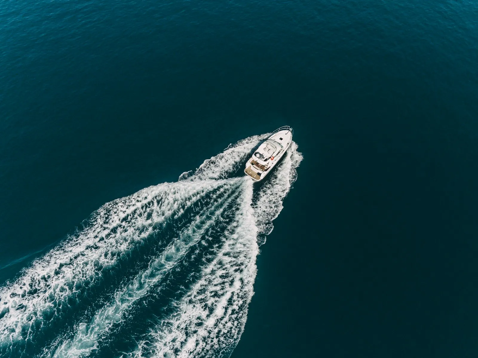 A white motorboat moving through deep blue water, leaving a large white wake