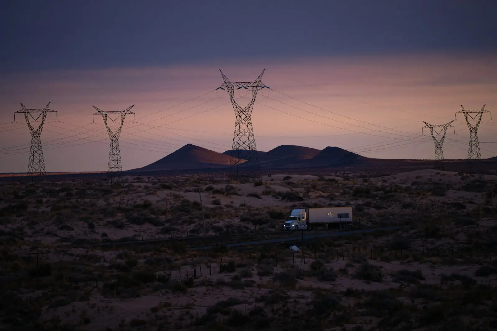 Power lines and truck in desolate landscape at dusk