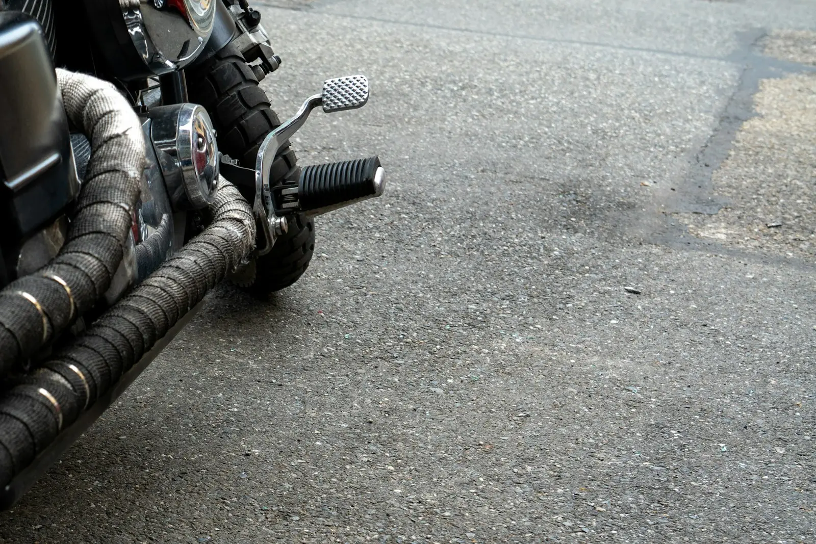 Motorcycle exhaust pipes and foot peg on asphalt