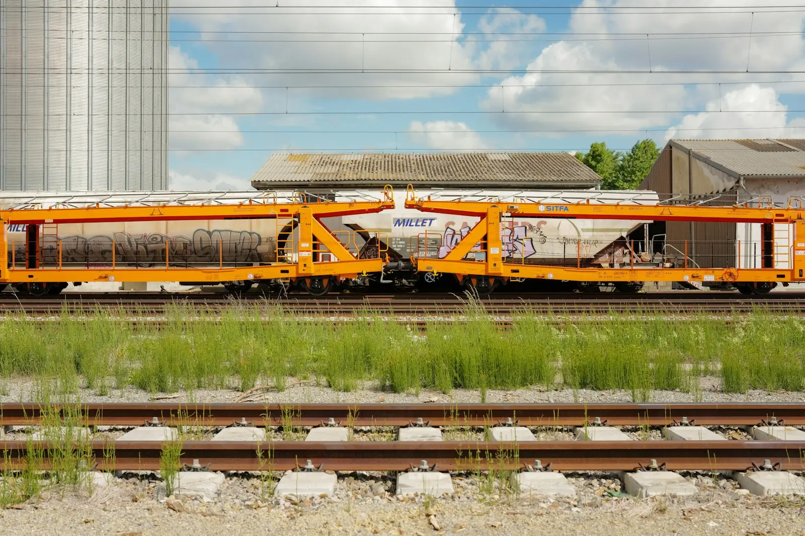 Orange train cars on tracks near a silo
